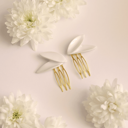 Contemporary porcelain jewellery: elegant bridal hair pins. Asymmetric white porcelain hairpins – two delicate leaves, each. Beautiful detail to minimal brides. Product close-up surrounded by natural white flowers.