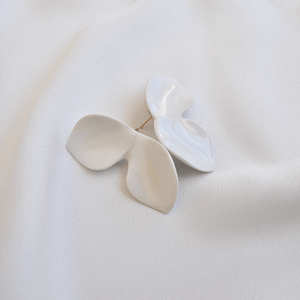 Product close-up: white porcelain earrings. Composition reminds a butterfly shape. White soft silk backgroun