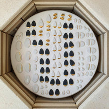 Load image into Gallery viewer, Kiln layer full of white and black porcelain pieces with gold details. 