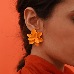 A stylish woman wearing a red blouse and showcasing a pair of strong orange porcelain earrings against a matching orange backdrop.
