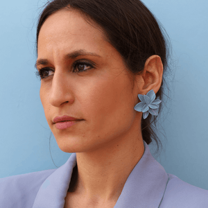 A stylish woman wearing a blue blazer and showcasing a pair of blue porcelain earrings against a matching blue backdrop.