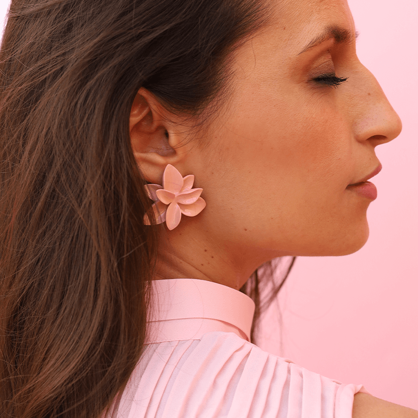 A stylish woman with her eyes closed wearing a soft pink blouse and showcasing a pair of delicate soft pink porcelain earrings against a matching soft pink backdrop.