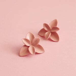 Nature-inspired jewellery: a delicate and romantic pair of soft pink porcelain earrings on a soft pink background. A detailed close-up shows the unique artisanal work.