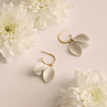 Load image into Gallery viewer, Light background for two beautiful white ceramic earrings. They seem like delicate white flowers. Bridal modern earrings surrounded by natural flowers. 