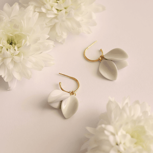 Light background for two beautiful white ceramic earrings. They seem like delicate white flowers. Bridal modern earrings surrounded by natural flowers. 