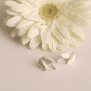 Modern jewelry: delicate white earrings  made of porcelain, surrounded by natural white flowers. Light background.
