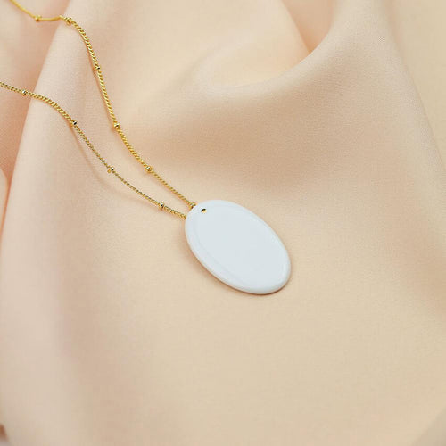 Exquisite white porcelain pendant on an elegant gold plated chain. Luminous product photography.