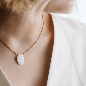 White pendant with a hand painted gold detail. Gold plated chain. Close-up of a minimal jewel.