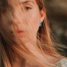 Load image into Gallery viewer, Light earrings made of soft blue porcelain. Minimalist jewellery conceived as wearable art.  Golden hour portrait of a blond woman. 