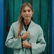 Load image into Gallery viewer, An elegant portrait of a woman wearing light blue porcelain dangle-down earrings. The earrings are matching her blue jacket. She&#39;s standing in front of a blue door.