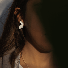 Load image into Gallery viewer, White ceramic earrings illuminated by the warm light of the golden hour.