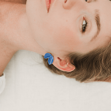 Load image into Gallery viewer, Beautiful portrait of a blond woman wearing delicate strong blue earrings. She has green eyes and is lying down on a white background.