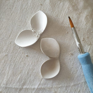Ceramics' studio scene: two raw porcelain pieces aside, shaped by hand using a fine brush.
